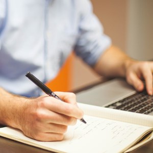 Person writing on notepad whilst using a laptop