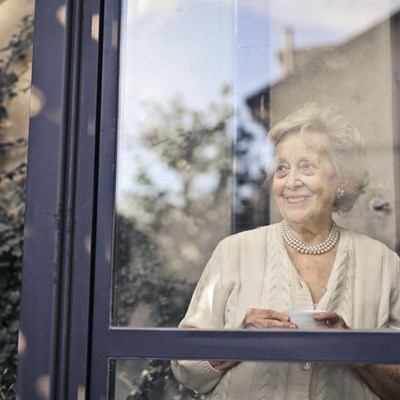 An older woman standing at a window. Stock photo
