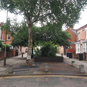 A brick planter and large tree at the end of a road