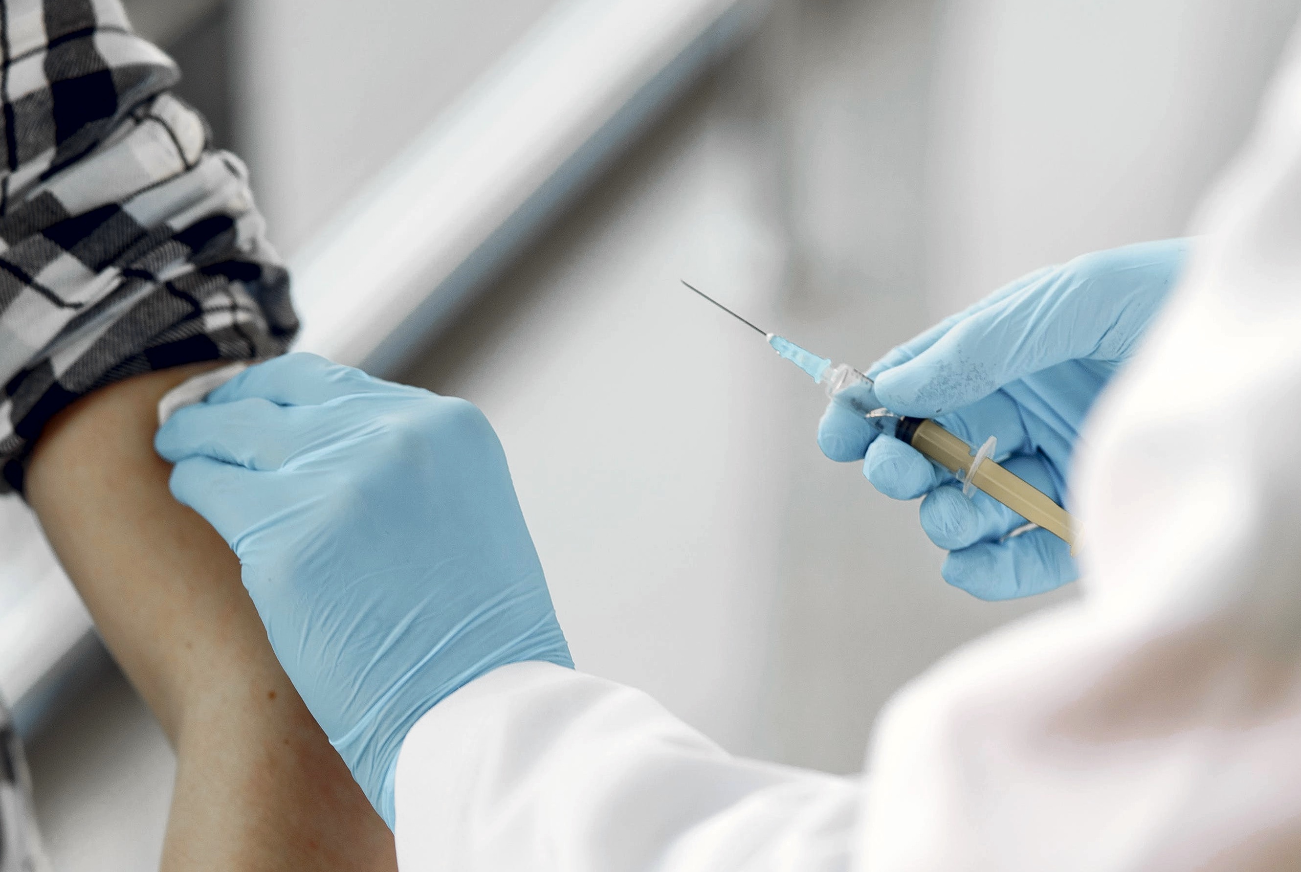 A medical professional wearing blue gloves holds a needle near a person's arm.