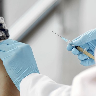 A medical professional wearing blue gloves holds a needle near a person's arm.