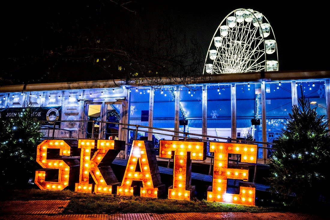 Illuminated Christmas ice rink sign with the Wheel of Light in background