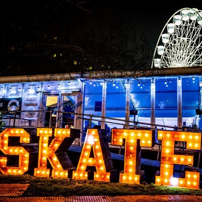 Illuminated Christmas ice rink sign with the Wheel of Light in background