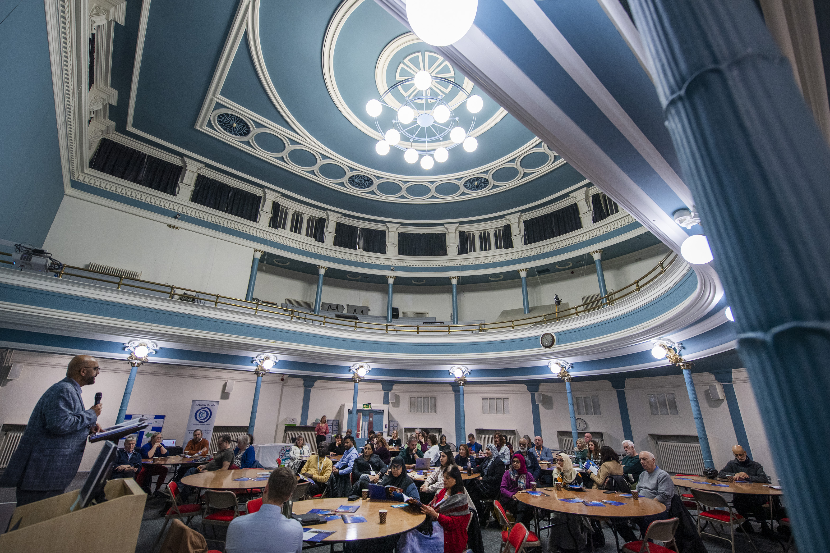 The blue elaborate ceiling of hansom Hall with groups of people seated at round tables beneath it.