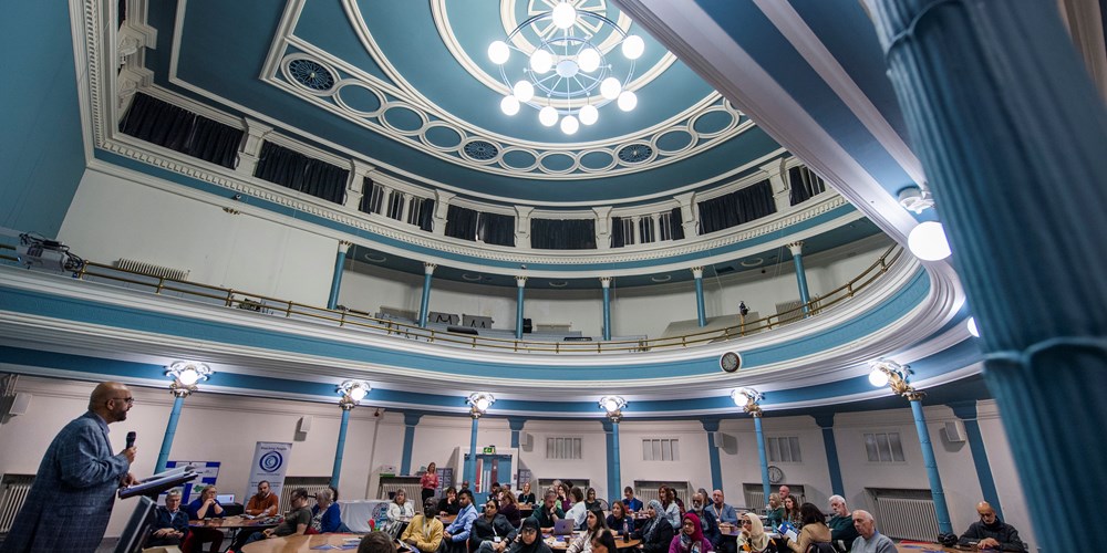 The blue elaborate ceiling of hansom Hall with groups of people seated at round tables beneath it.