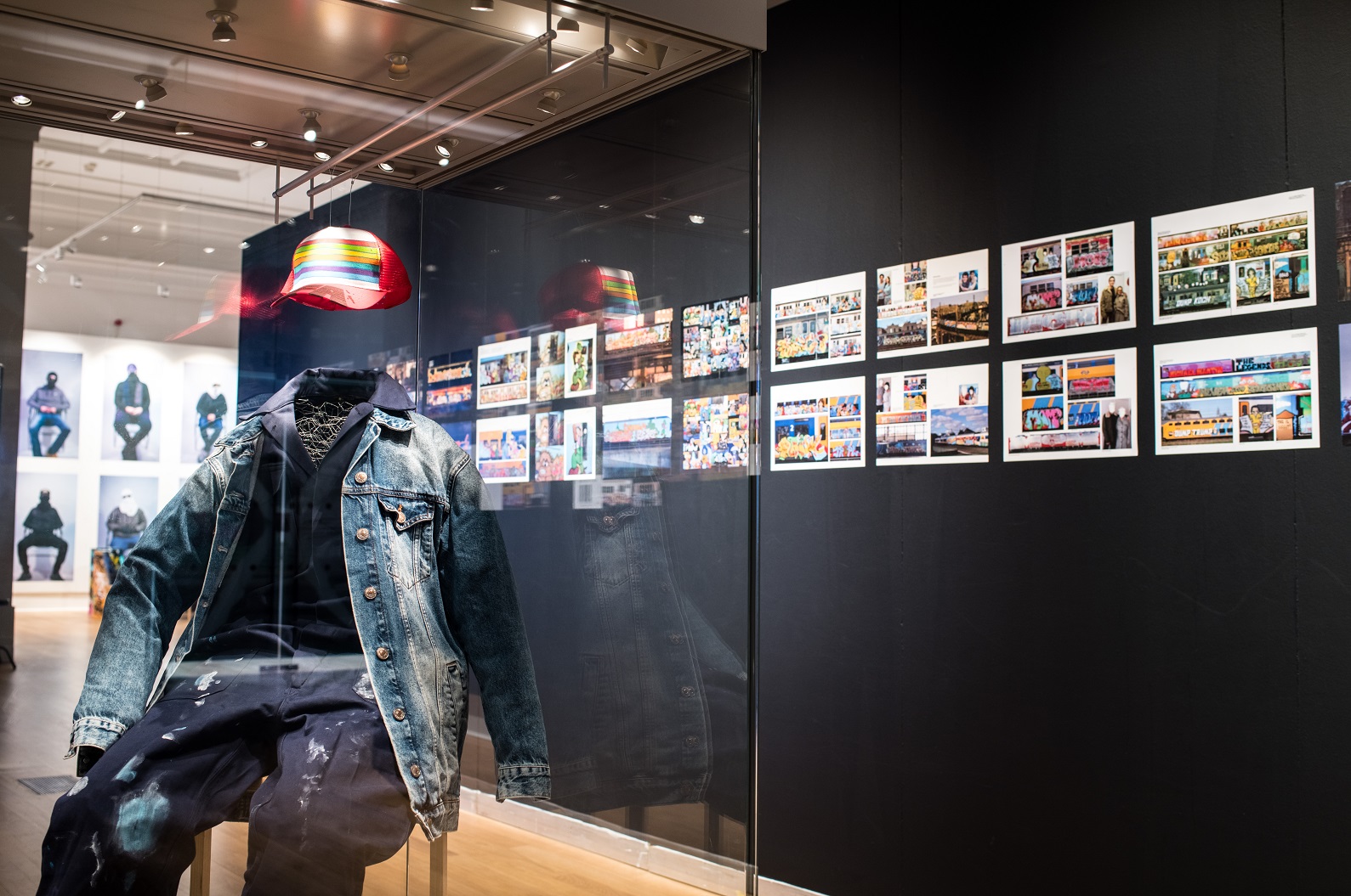 a view of the exhibition with photos in the background on a black screen and a graffiti artist's clothes in the foreground.
