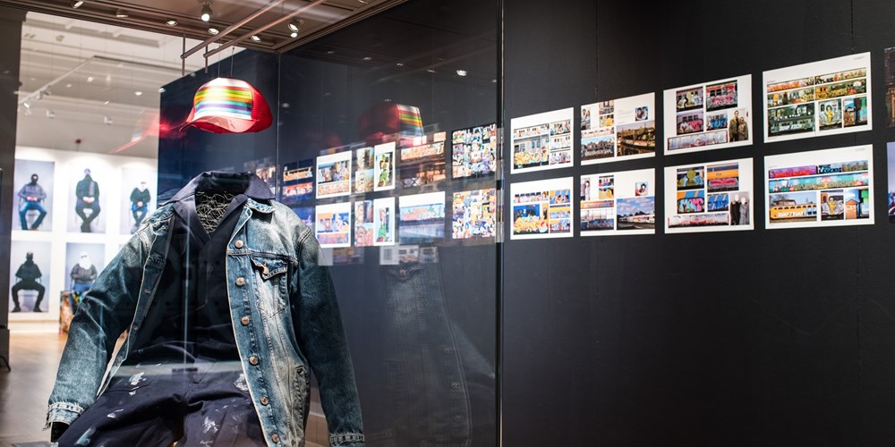 a view of the exhibition with photos in the background on a black screen and a graffiti artist's clothes in the foreground.