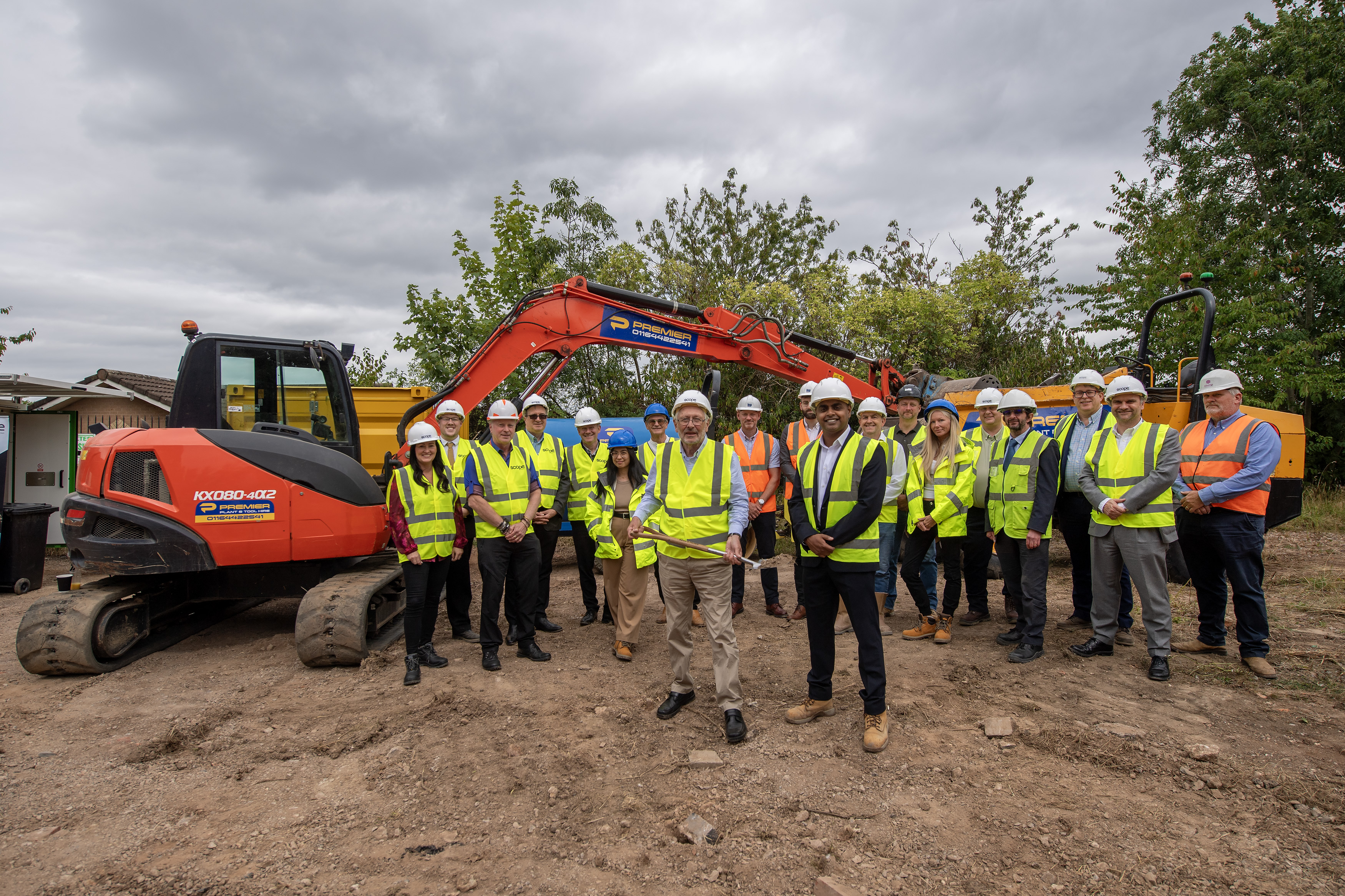 A large group of people wearing hard hats on a construction site with a digger in the background