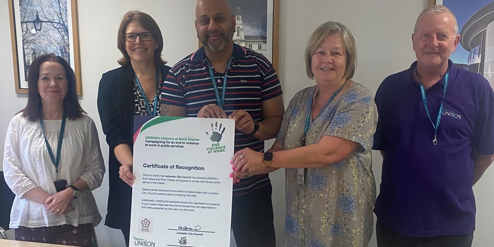 Three women and two women stand behind a large charter document.