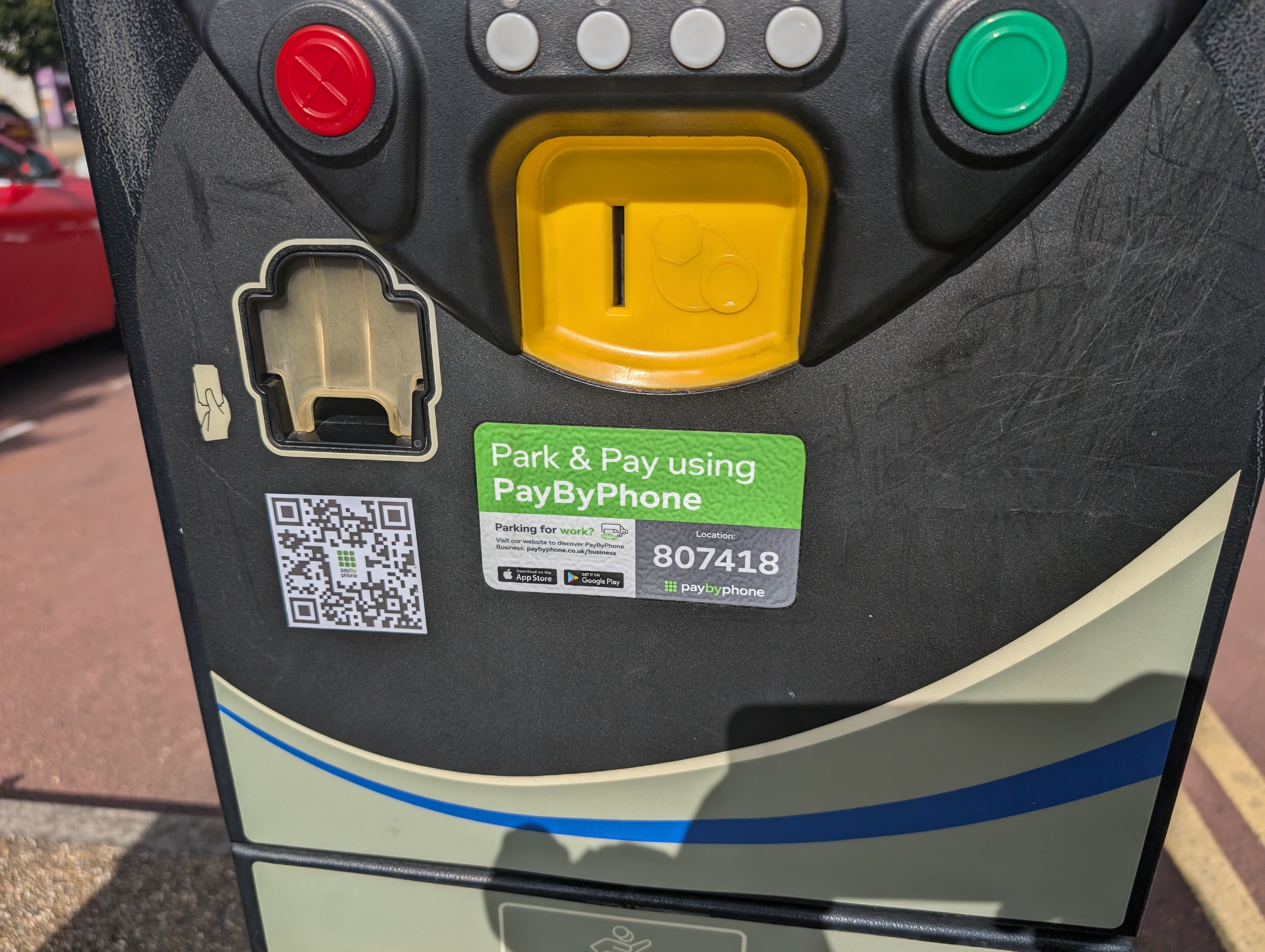 A grey parking payment machine with a QR code stuck on the front