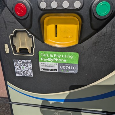 A grey parking payment machine with a QR code stuck on the front