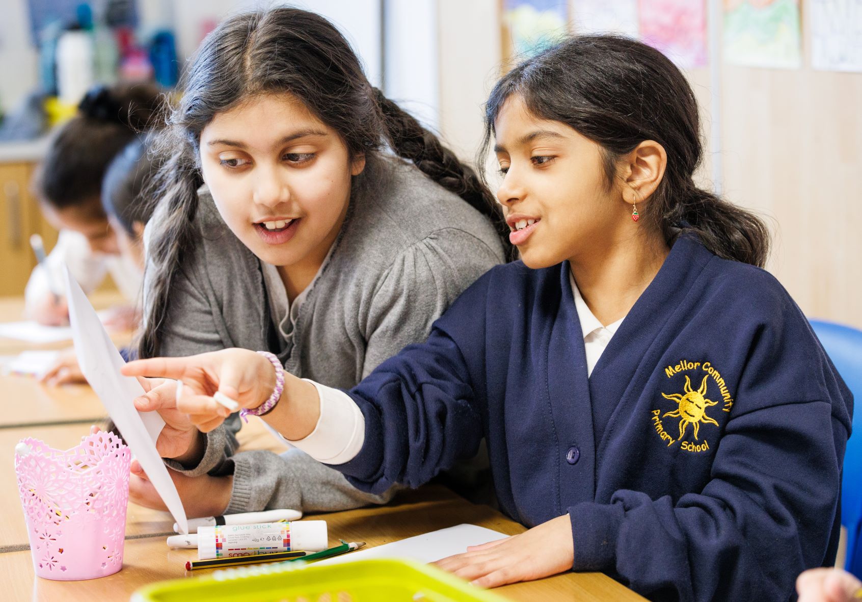 Two school girls both reading a text and pointing at the words