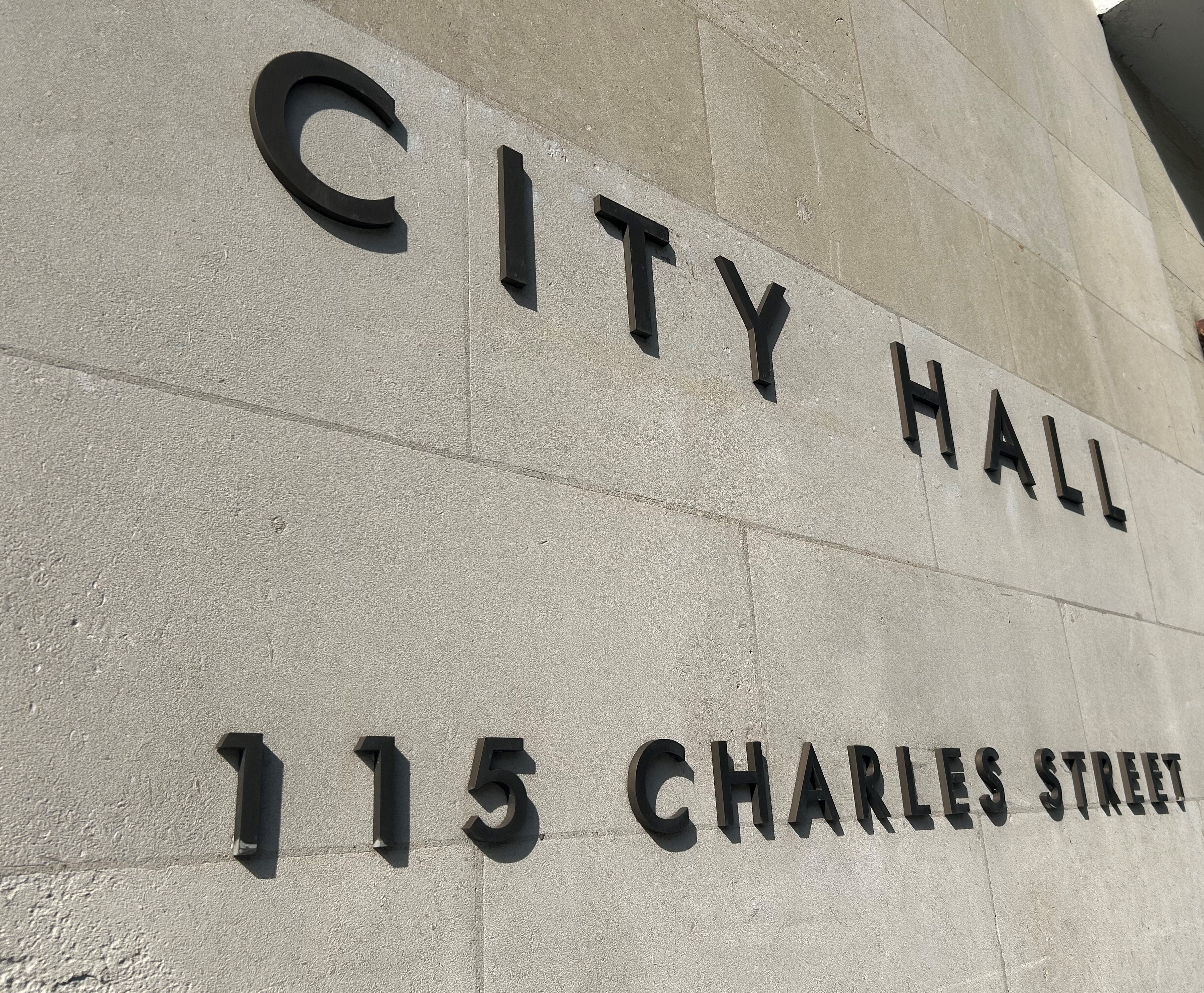 A cream stone wall with black letters spelling out City hall, 115 Charles Street