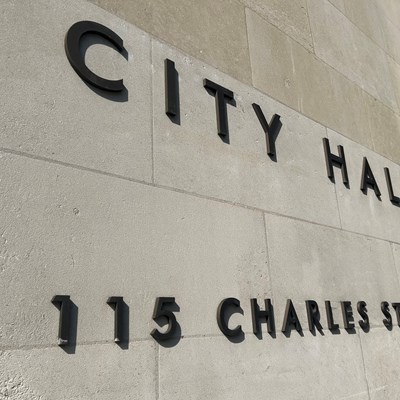A cream stone wall with black letters spelling out City hall, 115 Charles Street