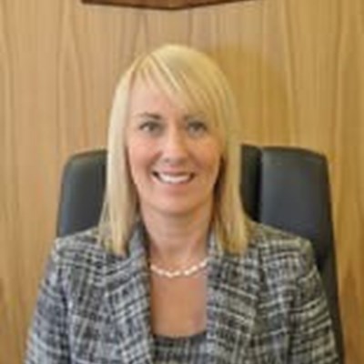 The coroner,  a blonde haired woman in a suit sits beneath the Leicester crest.