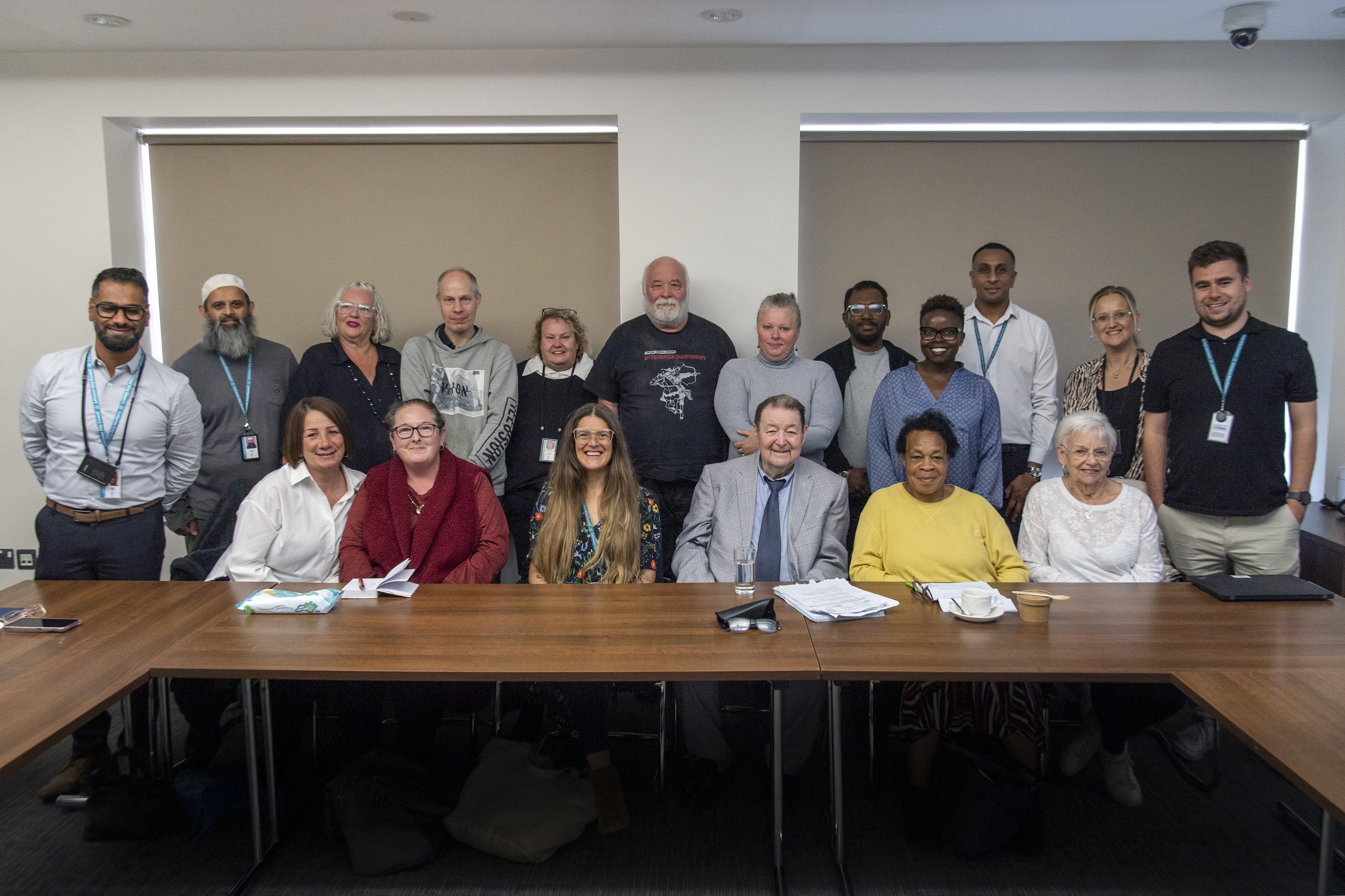 A large group of people sitting and standing behind a desk in a meeting room
