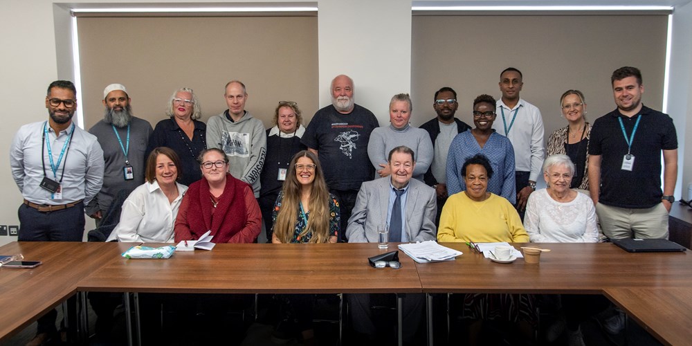 A large group of people sitting and standing behind a desk in a meeting room