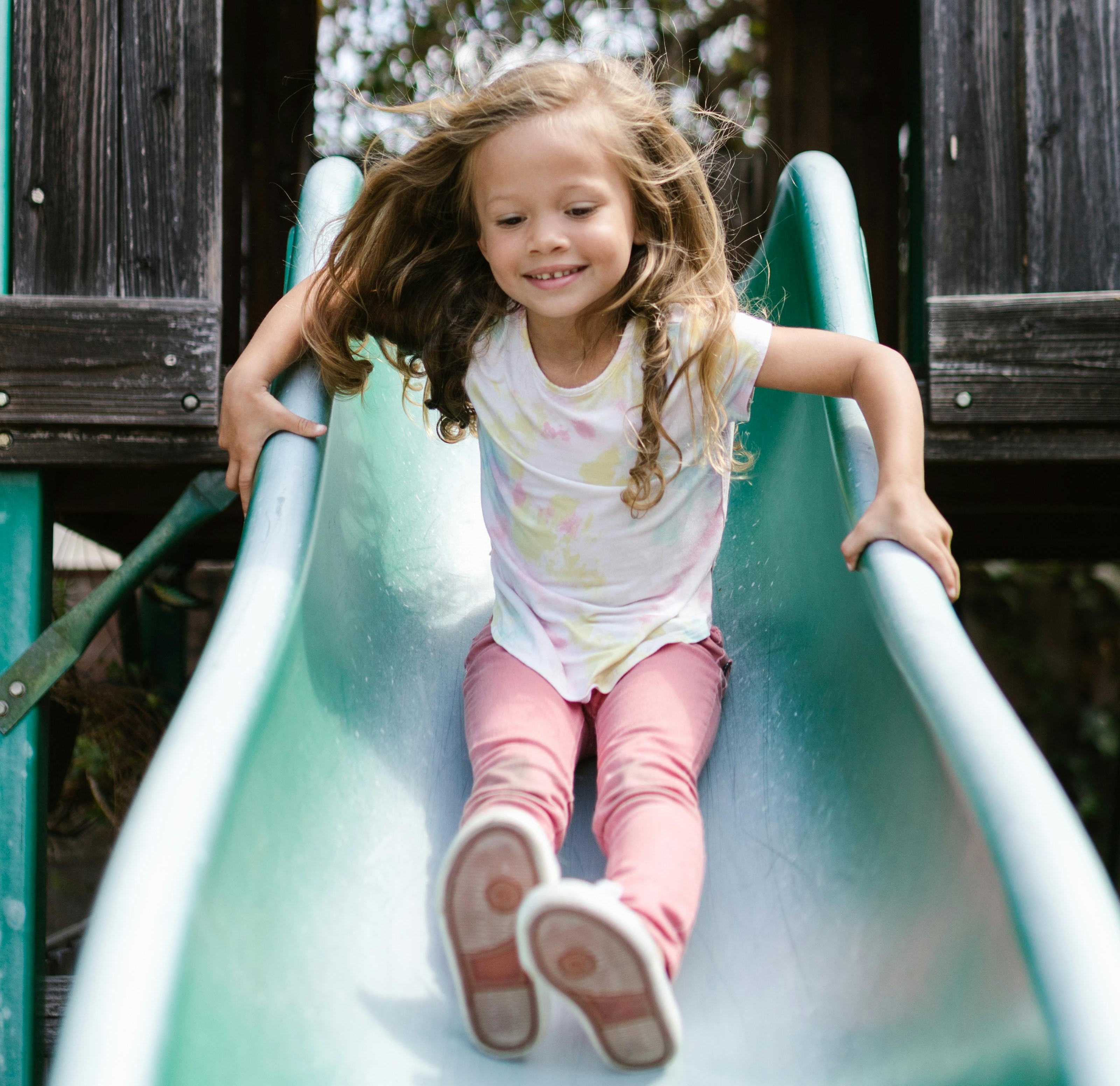 A young girl with long hair smiling as she goes down a slide