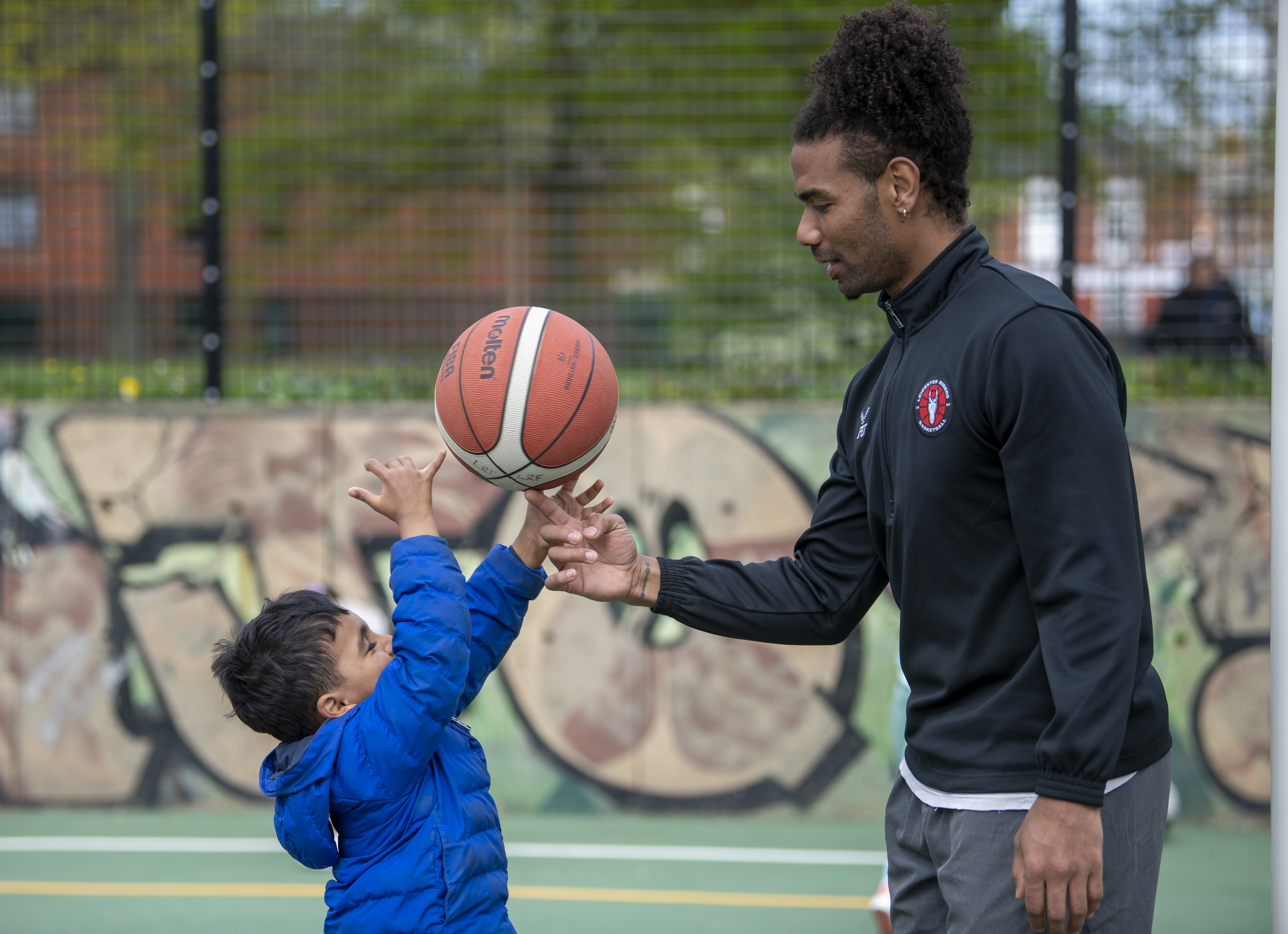 A Leicester Riders Foundation coach with a young child and basketball at Orchardson Avenue multi-use games area