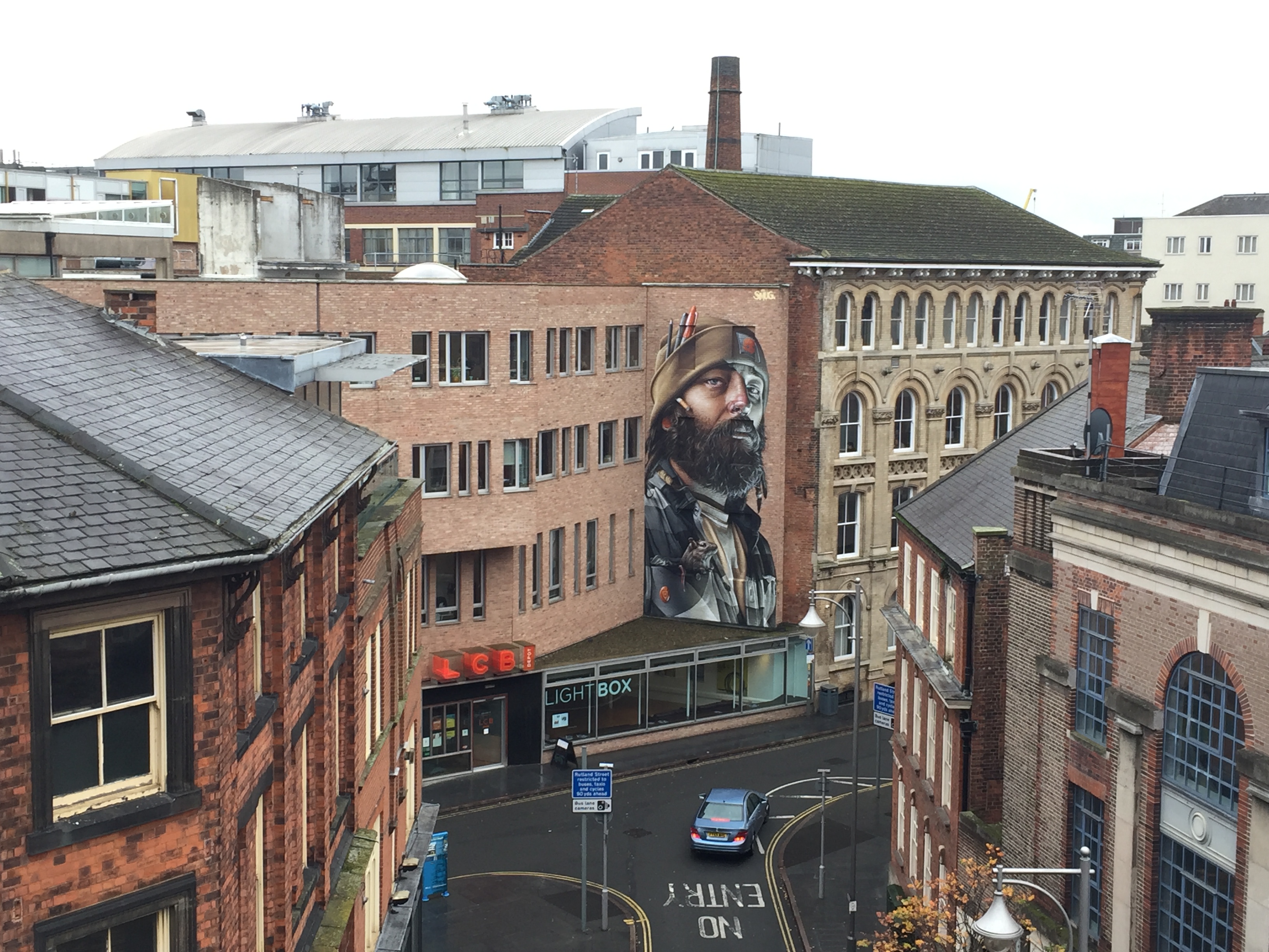 A view of tall buildings with a road between them, and a large painted mural on one wall.