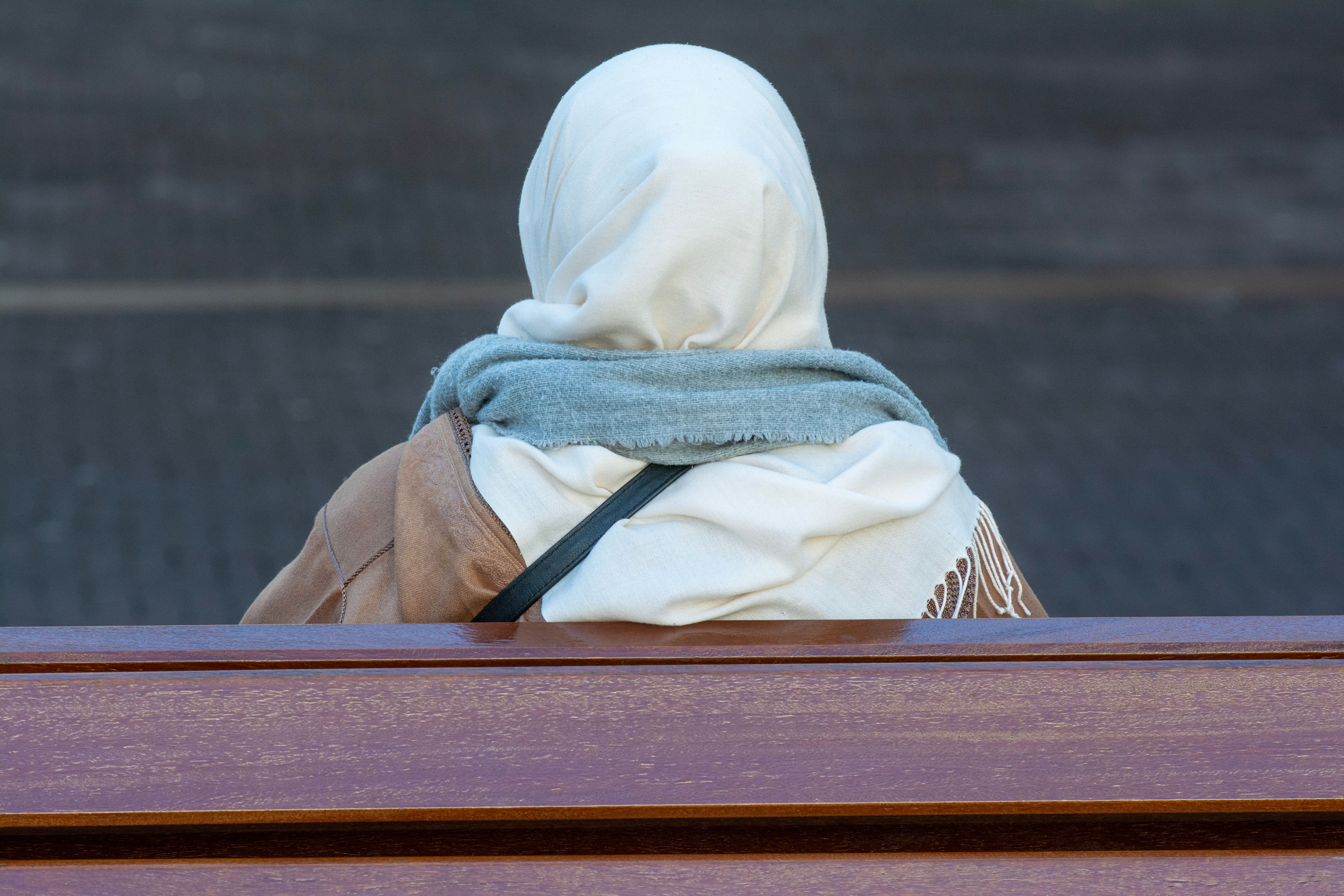 A Woman wearing a headscarf, sitting on a bench, pictured from the back.